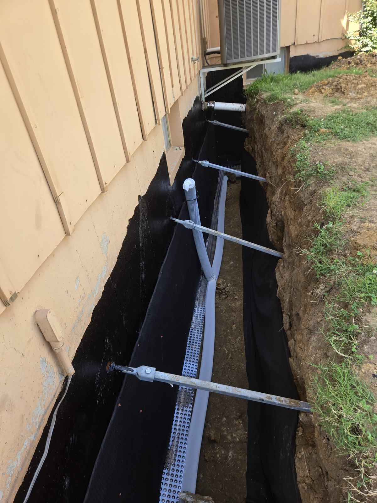 Exterior waterproofing membrane, drain tile and wall anchors along a basement wall